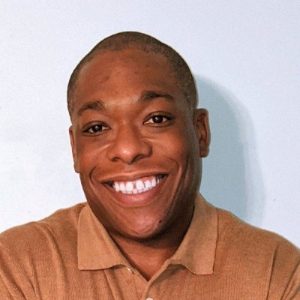 Headshot of LJ Nelson, he is wearing a light brown polo shirt and smiling
